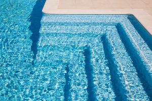 Swimming pool steps in the morning sunlight with shadows accentuating their pleasant curved shapes. The steps are tiles with tiles of various shades of blue.