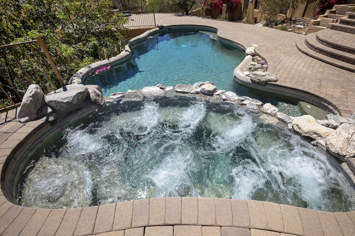 Hot tub with swimming pool and terraced patio at a luxury home in a desert environment.