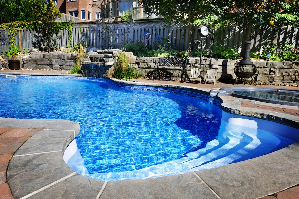 Residential inground swimming pool in backyard with waterfall and hot tub