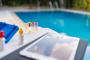 Swimming pool water quality checker kit with digital tablet by pool side.