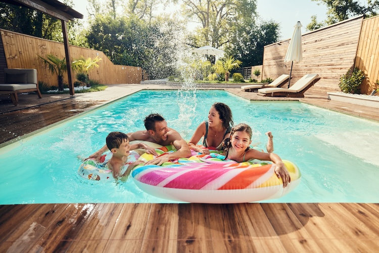 Carefree parents and their kids having fun during summer day in the swimming pool.