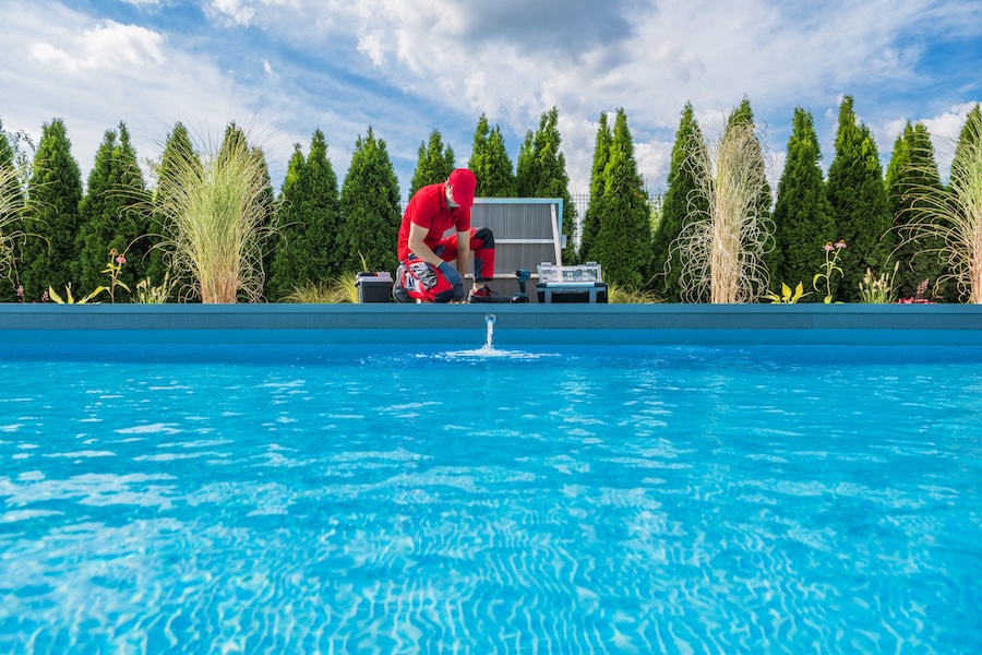 Professional Caucasian Swimming Pools Technician in His 40s Performing Seasonal Maintenance. Outdoor Residential Backyard Pool.